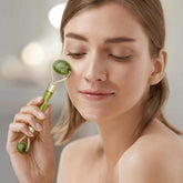 Woman using jade roller on face for skincare routine.