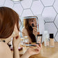 Woman using a white mini skincare fridge with mirror on makeup table.