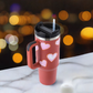 Thermos cup with handle and straw, featuring heart design on a blurred light background.