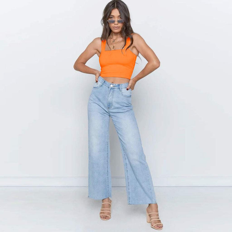 Woman wearing fluorescent orange sleeveless crop top with light blue jeans.